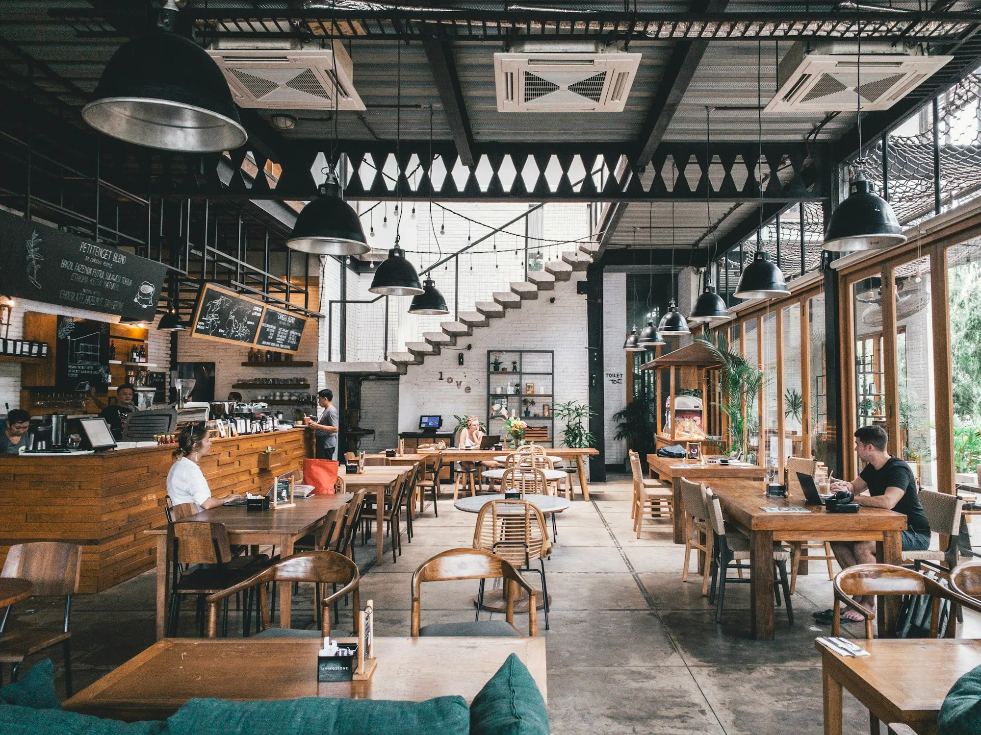 An airy restaurant with wooden tables under industrial lamps