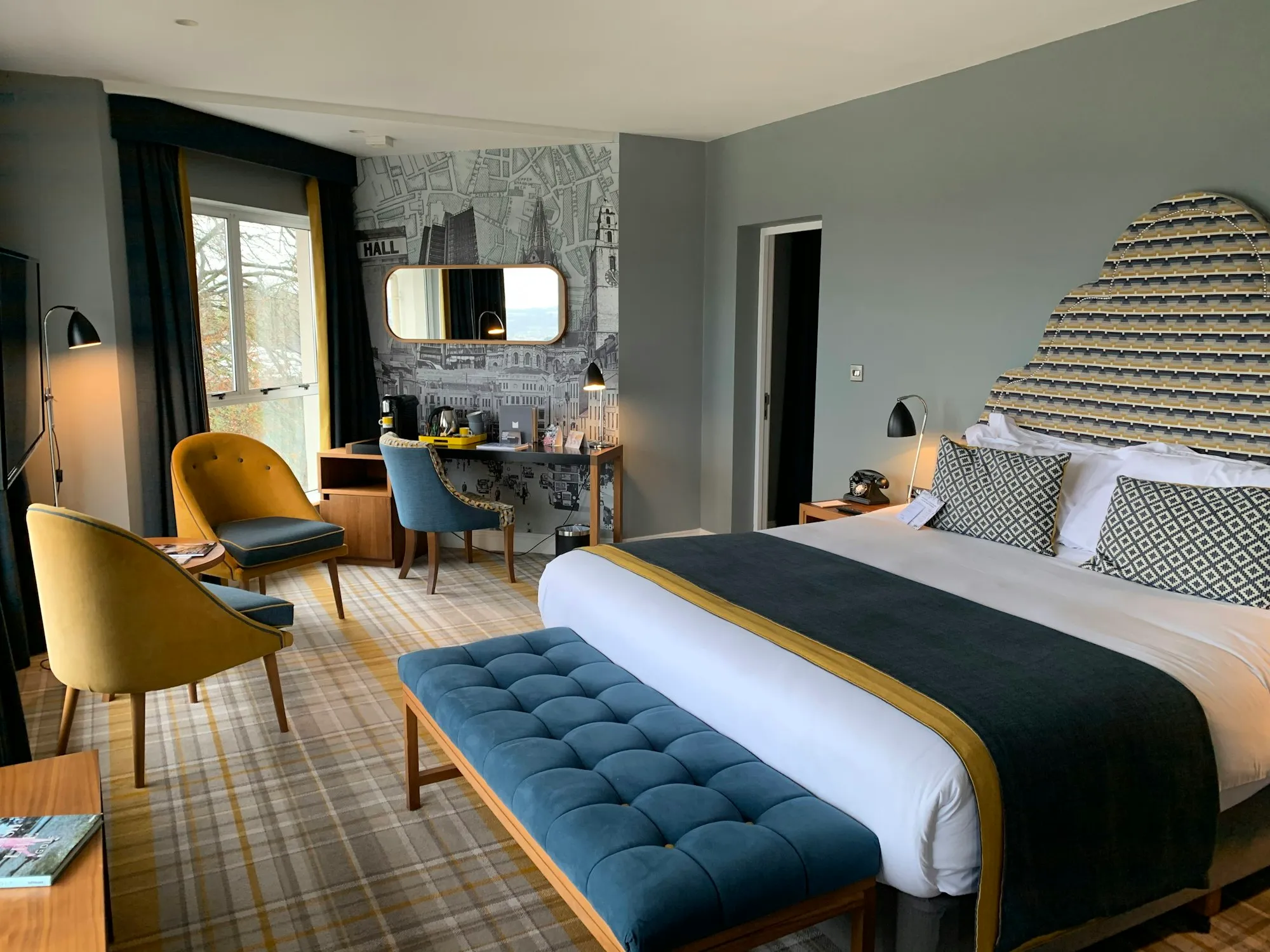 A bedroom with a mustard armchair, a navy bench and patterned headboard